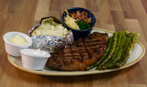 A grilled steak with asparagus, a baked potato, and a side salad, served on a white plate.