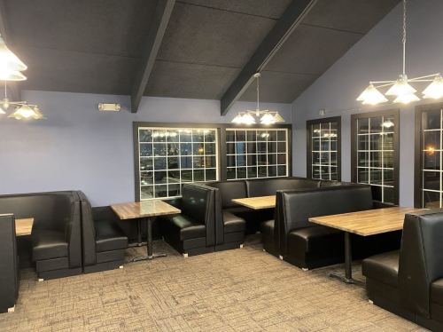 Interior of a restaurant featuring black booths and wooden tables, with large windows and a high ceiling.