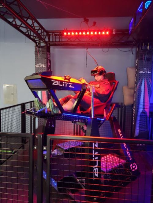 A person wearing a VR headset sits in a motion simulator, surrounded by lights and a safety enclosure.