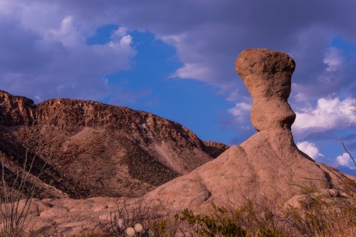 A unique rock formation resembling a figure, set against a backdrop of hills and a cloudy sky.