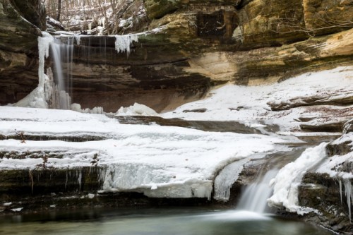 A serene winter scene featuring cascading waterfalls and icy rock formations in a forested area.