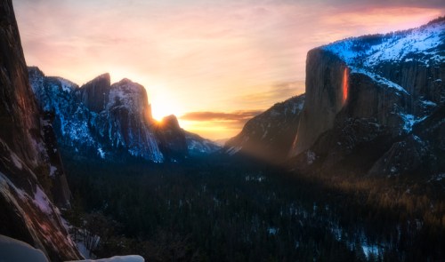 Sunset over a snowy mountain landscape, with dramatic cliffs and a valley illuminated by warm light.