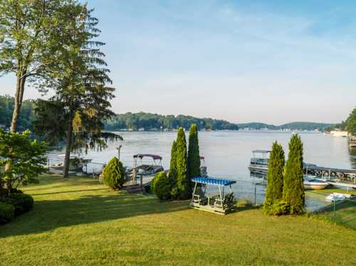 Scenic view of a calm lake surrounded by trees and boats, with a green lawn in the foreground.