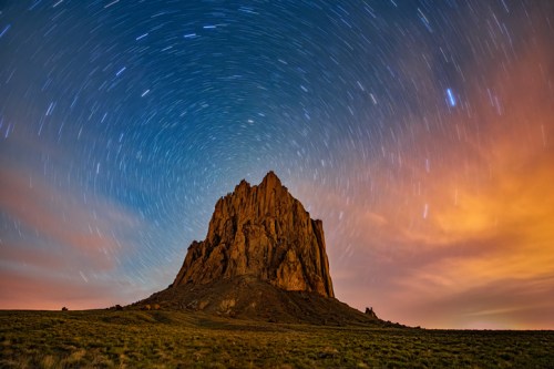 A towering rock formation under a starry sky with swirling stars and a hint of orange clouds at dusk.