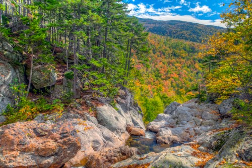 A scenic view of a rocky landscape surrounded by vibrant autumn foliage and a clear blue sky.