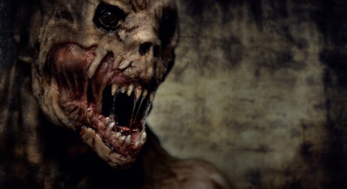 A grotesque creature with sharp teeth and a distorted face, set against a dark, textured background.