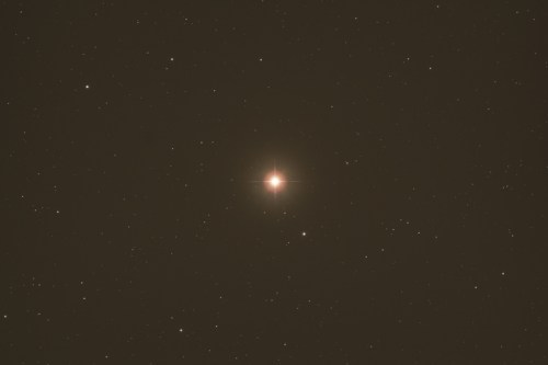 A bright star surrounded by a field of faint stars against a dark sky.
