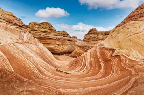 Colorful, swirling rock formations in a desert landscape under a blue sky with scattered clouds.