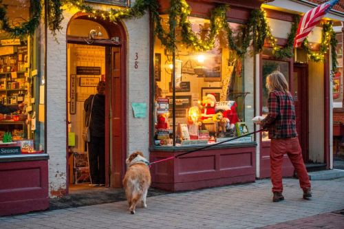 A person walks a dog past a festive shop decorated for the holidays, with lights and a Santa display in the window.