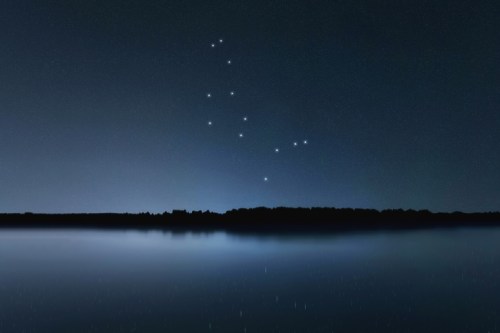 A serene night sky with stars forming a constellation above a calm, reflective body of water.