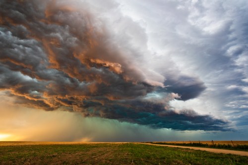 Dramatic storm clouds loom over a vast, open field, with a mix of dark and vibrant colors in the sky.