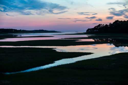 A serene landscape at dusk, featuring a winding river reflecting colorful clouds and a tranquil marsh.