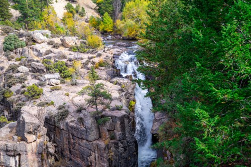 A scenic waterfall cascading over rocky cliffs, surrounded by lush greenery and autumn-colored trees.