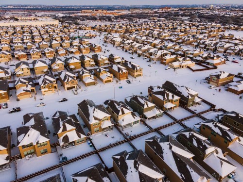 Aerial view of a snow-covered suburban neighborhood with rows of houses and streets visible.