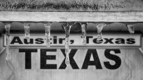 Icicles hanging from a structure with a sign reading "Austin, Texas" in the background, captured in black and white.