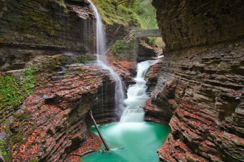 A serene waterfall cascades into a turquoise pool, surrounded by rocky cliffs and lush greenery.