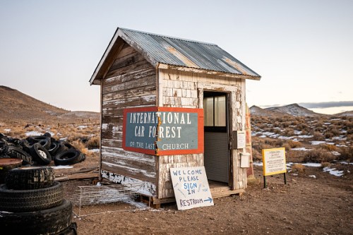 A small, weathered wooden building with signs for a "Cap Forest" and restroom, set in a barren landscape.