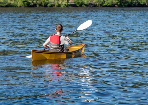 A person paddles a yellow kayak on a calm lake surrounded by greenery.