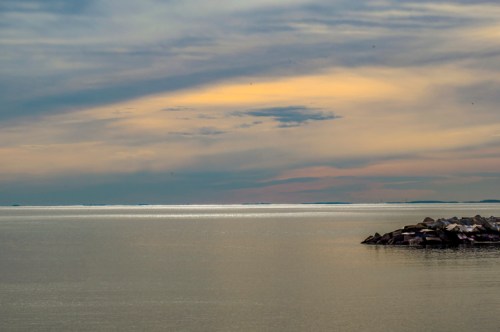 A serene seascape at dusk, featuring calm waters and a rocky shoreline under a colorful sky.