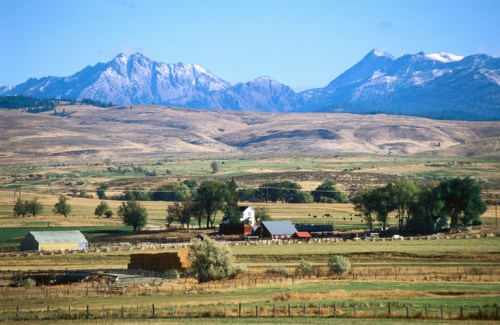 A scenic landscape featuring rolling hills, a farm with red barns, and snow-capped mountains in the background.