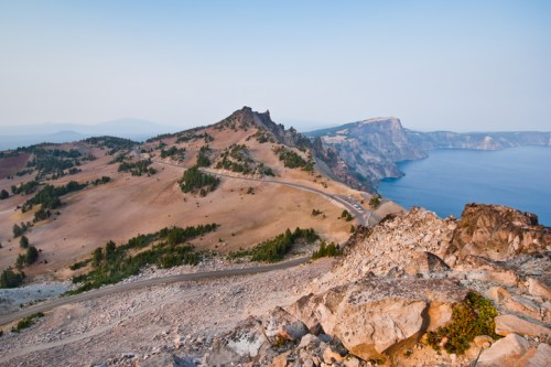 A scenic view of a rugged landscape with hills, trees, and a calm blue lake under a clear sky.