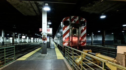 A train with a red and white striped front waits at a dimly lit underground station platform.