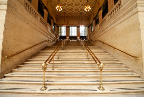 A grand staircase with marble steps and brass railings, leading to an ornate, well-lit upper level.