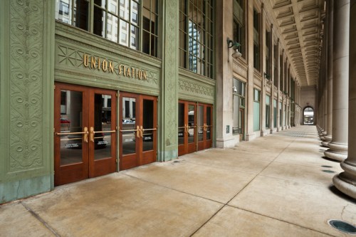 Exterior view of Union Station with ornate green walls and large wooden doors, featuring a wide, empty walkway.