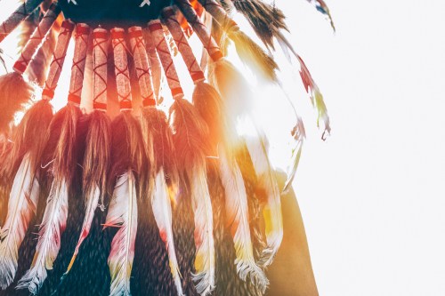 A close-up of a colorful feathered headdress against a bright background, showcasing intricate details and textures.