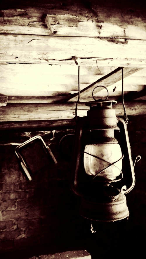 A vintage lantern hanging from a wooden ceiling, casting a warm glow in a rustic, dimly lit space.