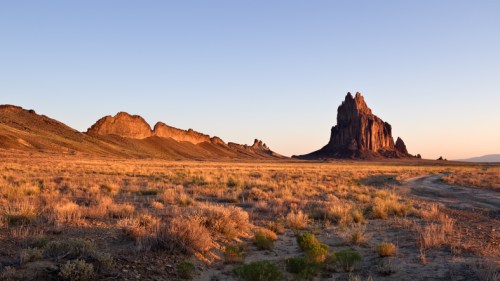 A scenic landscape featuring rugged rock formations and a vast, open field under a clear sky at sunset.