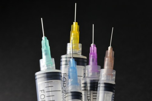 Five syringes with colorful needle caps arranged against a dark background.