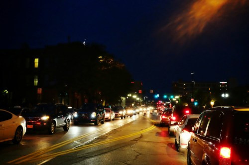 A busy street at night with rows of cars and traffic lights illuminating the scene.