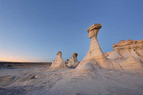 Unique rock formations rise against a clear blue sky at sunset, showcasing natural erosion in a desert landscape.