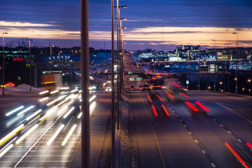 A busy highway at dusk, with streaks of light from moving vehicles and a colorful sunset in the background.