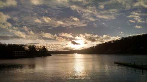 A serene lake at sunset, with clouds reflecting on the water and a silhouette of trees in the background.