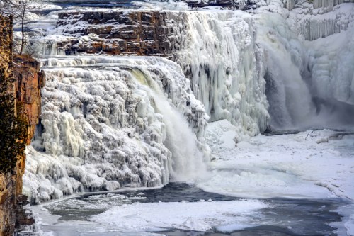 A frozen waterfall cascading over rocky cliffs, surrounded by ice and snow, creating a winter wonderland scene.