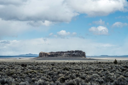 A flat-topped rock formation rises above a vast, open landscape under a cloudy sky.