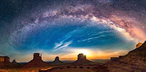 A stunning night sky filled with stars and the Milky Way arching over Monument Valley's iconic rock formations.