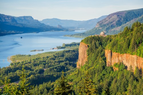 A scenic view of a river winding through lush green hills and cliffs under a clear blue sky.