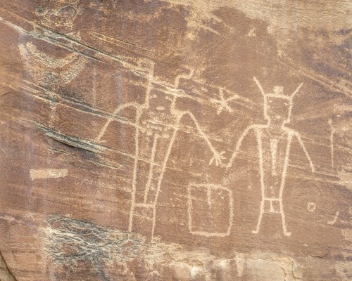 Petroglyphs on rock surface depicting two figures holding hands, with geometric shapes and symbols in the background.