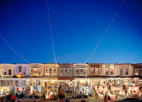 A row of houses adorned with colorful Christmas lights against a clear blue sky, creating a festive atmosphere.