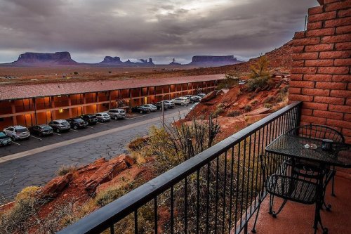 View from a balcony overlooking a parking lot and desert landscape with distant rock formations under a cloudy sky.