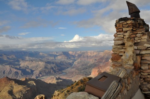 A scenic view of the Grand Canyon with rocky cliffs and a cloudy sky, featuring a stone structure in the foreground.