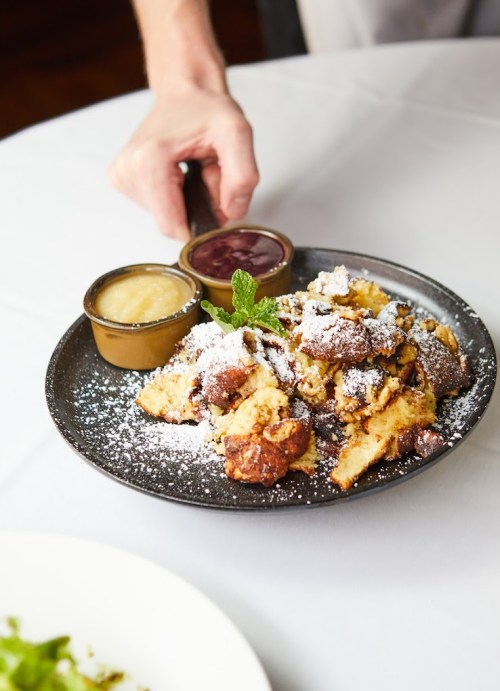 A plate of dessert with powdered sugar, served with two sauces, held by a hand.