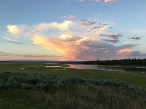 A serene landscape featuring a river winding through green fields under a colorful sunset sky with scattered clouds.