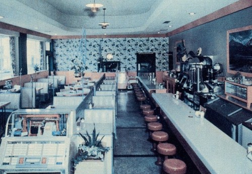 A retro diner interior with red stools, a long counter, jukebox, and floral wallpaper. Bright and inviting atmosphere.