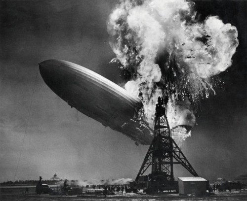 A zeppelin explodes in mid-air above a launch platform, surrounded by smoke and flames.