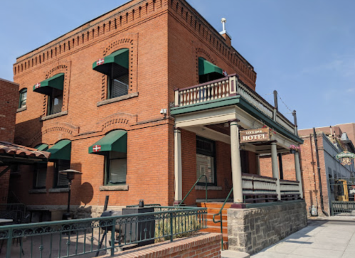 Historic brick hotel with green awnings and a porch, set against a clear blue sky.