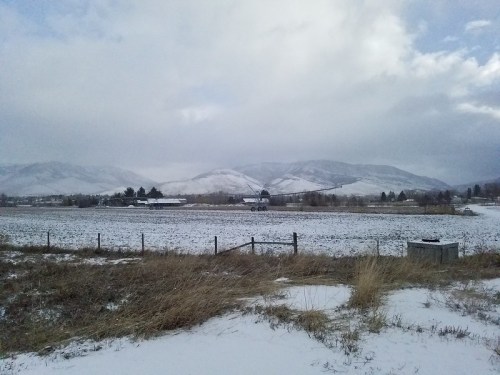 A snowy landscape with mountains in the background, a field in the foreground, and a cloudy sky above.
